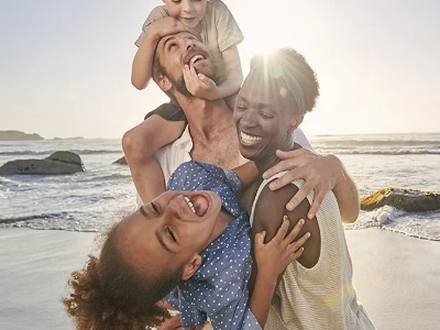 Famille souriante jouant ensemble sur une plage ensoleillée, avec la mer en arrière-plan.